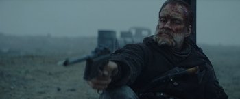 Movie still from “Sisu” (2022), directed by Jalmari Helander – A man holding a gun while sitting on the ground; Close Up shot, Over the shoulder angle
