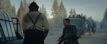 Movie still from “Sisu” (2022), directed by Jalmari Helander – Two men standing next to each other holding guns; Medium shot, Over the shoulder angle