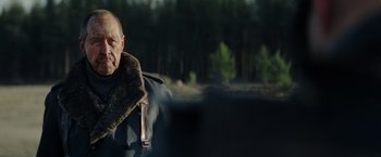 Movie still from “Sisu” (2022), directed by Jalmari Helander – An older man wearing a jacket and a fur collar; Close Up shot, Over the shoulder angle