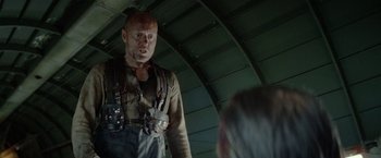 Movie still from “Sisu” (2022), directed by Jalmari Helander – A bald man with a beard is standing next to another bald man; Medium shot, Low angle