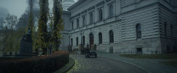 Movie still from “Sisu” (2022), directed by Jalmari Helander – A man riding a scooter down a street near a building; Extreme Wide shot, High angle