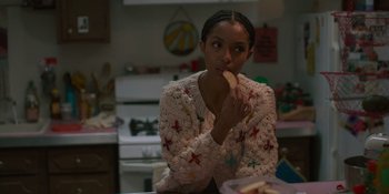 Movie still from “Sitting in Bars with Cake” (2023), directed by Trish Sie – A woman is eating a sandwich in a kitchen; Medium shot, Over the shoulder angle