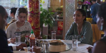 Movie still from “Sitting in Bars with Cake” (2023), directed by Trish Sie – Two people sitting at a table with food on it; Medium shot, Over the shoulder angle