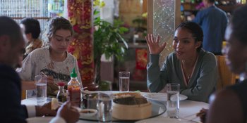 Movie still from “Sitting in Bars with Cake” (2023), directed by Trish Sie – A woman sitting at a dinner table with a child; Medium shot, Over the shoulder angle