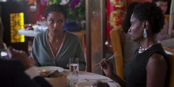 Movie still from “Sitting in Bars with Cake” (2023), directed by Trish Sie – A woman sitting at a table in front of two other people; Close Up shot, Over the shoulder angle