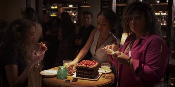 Movie still from “Sitting in Bars with Cake” (2023), directed by Trish Sie – A group of people standing around a table with a cake on it; Medium shot, Over the shoulder angle