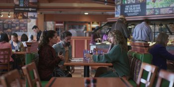 Movie still from “Sitting in Bars with Cake” (2023), directed by Trish Sie – A group of people sitting at a table with drinks; Wide shot, High angle