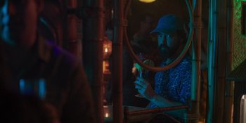 Movie still from “Sitting in Bars with Cake” (2023), directed by Trish Sie – A man sitting in front of a mirror holding a drink; Medium shot, Over the shoulder angle