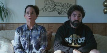Movie still from “Sitting in Bars with Cake” (2023), directed by Trish Sie – A man and a woman sitting next to each other on a couch; Medium shot, Over the shoulder angle