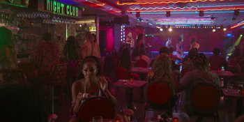Movie still from “Sitting in Bars with Cake” (2023), directed by Trish Sie – A group of people sitting at tables in a room; Extreme Wide shot, High angle