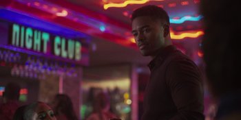 Movie still from “Sitting in Bars with Cake” (2023), directed by Trish Sie – A man standing in front of neon lights in a room; Close Up shot, Over the shoulder angle