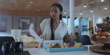 Movie still from “Sitting in Bars with Cake” (2023), directed by Trish Sie – A woman sitting in front of a box of cake; Medium shot, Over the shoulder angle