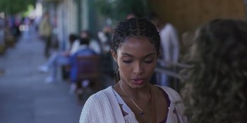 Movie still from “Sitting in Bars with Cake” (2023), directed by Trish Sie – A young woman with braids wearing a white sweater; Close Up shot, Over the shoulder angle