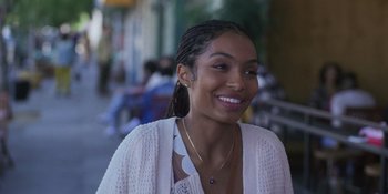 Movie still from “Sitting in Bars with Cake” (2023), directed by Trish Sie – A woman smiles while standing on the sidewalk; Close Up shot, Over the shoulder angle
