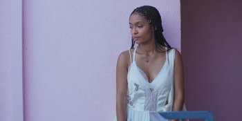 Movie still from “Sitting in Bars with Cake” (2023), directed by Trish Sie – A woman in a white dress standing in front of a pink wall; Close Up shot, Over the shoulder angle