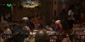 Movie still from “Sitting in Bars with Cake” (2023), directed by Trish Sie – A group of people sitting at a table with food; Medium shot, Over the shoulder angle