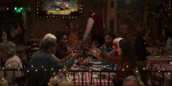 Movie still from “Sitting in Bars with Cake” (2023), directed by Trish Sie – A group of people sitting at a table drinking wine; Wide shot, Over the shoulder angle