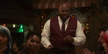 Movie still from “Sitting in Bars with Cake” (2023), directed by Trish Sie – A man holding a pan in front of a woman sitting down; Medium shot, Over the shoulder angle