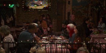 Movie still from “Sitting in Bars with Cake” (2023), directed by Trish Sie – A group of people sitting at a table with plates of food on it; Wide shot, High angle