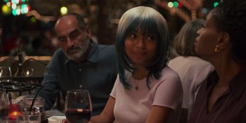 Movie still from “Sitting in Bars with Cake” (2023), directed by Trish Sie – A woman sitting at a table with a glass of red wine; Medium shot, Over the shoulder angle