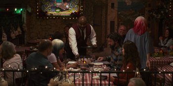 Movie still from “Sitting in Bars with Cake” (2023), directed by Trish Sie – A group of people sitting around a table with plates of food on it; Wide shot, Over the shoulder angle