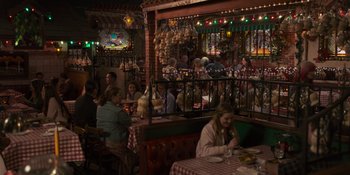 Movie still from “Sitting in Bars with Cake” (2023), directed by Trish Sie – People are sitting at tables in a restaurant; Wide shot, High angle