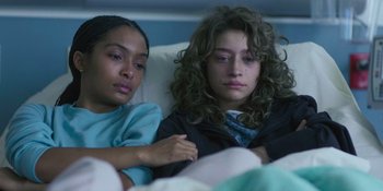 Movie still from “Sitting in Bars with Cake” (2023), directed by Trish Sie – Two people sitting in a bed with one of them looking at the camera; Medium shot, High angle