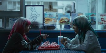 Movie still from “Sitting in Bars with Cake” (2023), directed by Trish Sie – Two people sitting at a table eating food; Medium shot, High angle