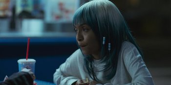 Movie still from “Sitting in Bars with Cake” (2023), directed by Trish Sie – A woman with blue hair is sitting in a room; Close Up shot, Over the shoulder angle