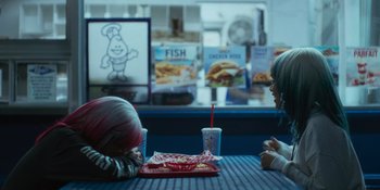 Movie still from “Sitting in Bars with Cake” (2023), directed by Trish Sie – Two people sitting at a table with a drink; Medium shot, Over the shoulder angle