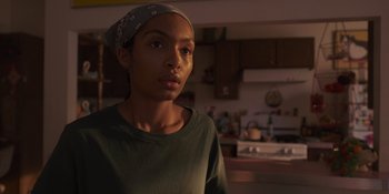 Movie still from “Sitting in Bars with Cake” (2023), directed by Trish Sie – A woman with a bandanna is standing in a kitchen; Close Up shot, Low angle