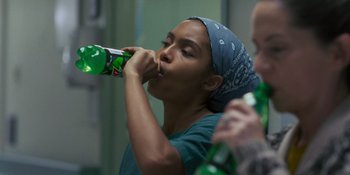 Movie still from “Sitting in Bars with Cake” (2023), directed by Trish Sie – A woman with a bandanna on drinking a soda; Medium shot, Over the shoulder angle