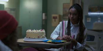 Movie still from “Sitting in Bars with Cake” (2023), directed by Trish Sie – A woman sitting in front of a cake on a table; Medium shot, Over the shoulder angle