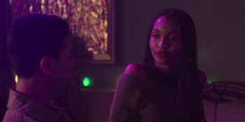 Movie still from “Sitting in Bars with Cake” (2023), directed by Trish Sie – A woman with braids sitting in a dark room; Close Up shot, Over the shoulder angle