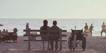 Movie still from “Sitting in Bars with Cake” (2023), directed by Trish Sie – Two people sitting on a bench looking out at the ocean; Wide shot, High angle
