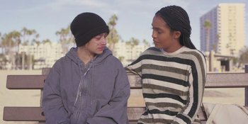 Movie still from “Sitting in Bars with Cake” (2023), directed by Trish Sie – Two young people sitting next to each other on a park bench; Medium shot, Over the shoulder angle
