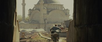 Movie still from “Skyfall” (2012), directed by Sam Mendes – A man riding a motorcycle down the middle of a street; Extreme Wide shot, Low angle