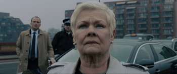 Movie still from “Skyfall” (2012), directed by Sam Mendes – An older woman is standing in front of a car; Close Up shot, Low angle