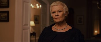 Movie still from “Skyfall” (2012), directed by Sam Mendes – An older woman wearing a black dress and a pearl necklace; Close Up shot, Low angle