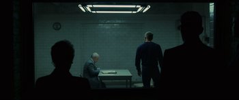 Movie still from “Skyfall” (2012), directed by Sam Mendes – Two men standing in front of a table in a dark room; Wide shot, Over the shoulder angle