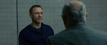 Movie still from “Skyfall” (2012), directed by Sam Mendes – A man standing next to another man in front of a brick wall; Close Up shot, Over the shoulder angle