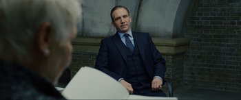Movie still from “Skyfall” (2012), directed by Sam Mendes – A man in a suit sitting in front of another man in a suit; Medium shot, Over the shoulder angle