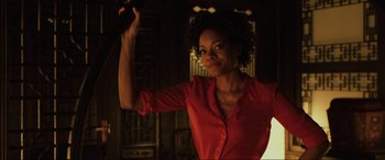 Movie still from “Skyfall” (2012), directed by Sam Mendes – A woman in a red shirt is holding something in her hand; Medium shot, Low angle