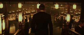 Movie still from “Skyfall” (2012), directed by Sam Mendes – A man in a suit standing in front of a group of people in a room; Wide shot, Over the shoulder angle