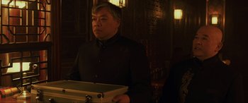 Movie still from “Skyfall” (2012), directed by Sam Mendes – A man in a suit holding a box in a dark room; Medium shot, Over the shoulder angle