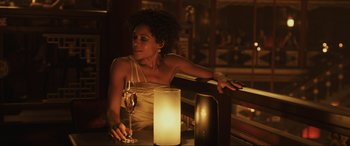 Movie still from “Skyfall” (2012), directed by Sam Mendes – A woman sitting at a table holding a glass of wine; Medium shot, Over the shoulder angle