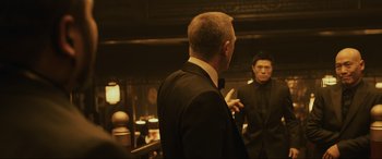 Movie still from “Skyfall” (2012), directed by Sam Mendes – A man in a suit and tie standing next to another man in a suit and tie; Medium shot, Over the shoulder angle