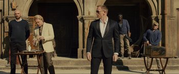 Movie still from “Skyfall” (2012), directed by Sam Mendes – A man in a suit and sunglasses standing in front of a building; Medium shot, Over the shoulder angle