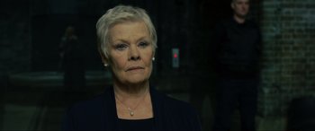 Movie still from “Skyfall” (2012), directed by Sam Mendes – An older woman with short blonde hair wearing a black jacket; Close Up shot, Low angle