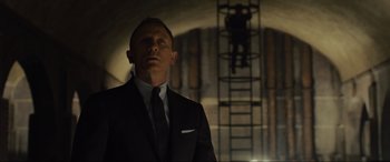 Movie still from “Skyfall” (2012), directed by Sam Mendes – A man in a suit and tie standing in front of a ladder; Medium shot, Low angle